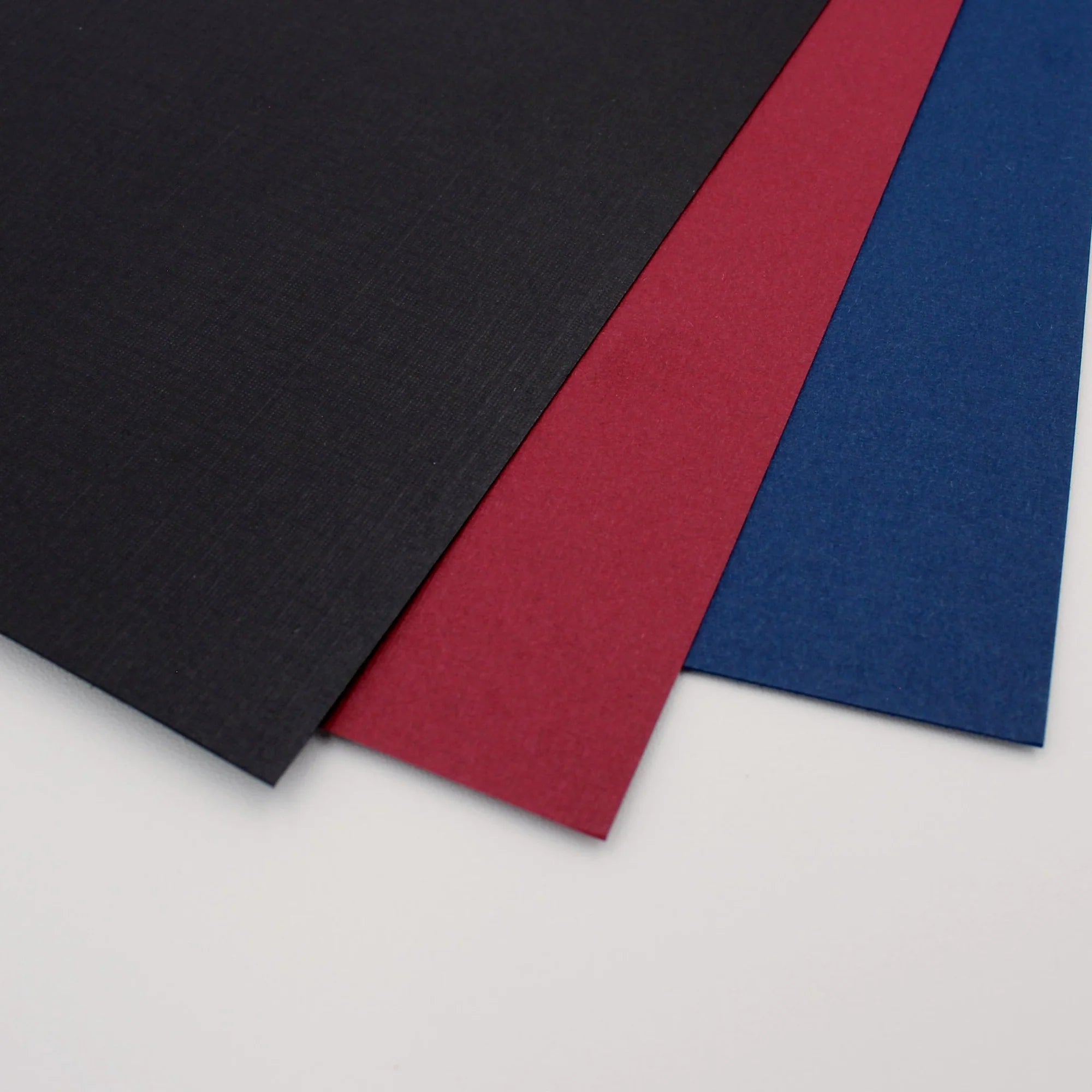 Three sheets of colored cover sets paper in black, red, and blue on a light gray background