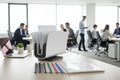 Desk with office supplies and people working in the background Peleman binder 8.2 UK