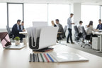 Desk with office supplies and people working in the background Peleman binder 8.2 UK